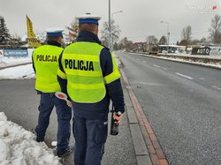 Zdjęcie kolorowe zrobione w zimie dwóch policjantów stoi tyłem w tle ulica