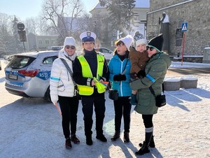 zdjęcie grupowe policjantka trzyma odblaski obok niej stoją osoby w tle radiowóz