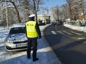 policjant w rejonie przejścia dla pieszych w tle radiowóz oraz jadące samochody