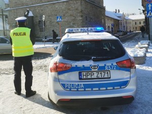 policjant stoi tyłem obok radiowóz w tle przejście dla pieszych