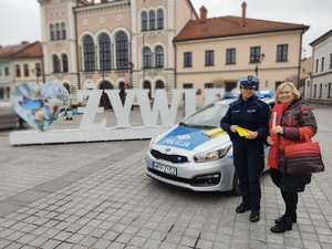zdjęcie kolorowe zrobione na rynku w Żywcu obok radiowozu stoi policjantka z kobietą i trzymają odblaski