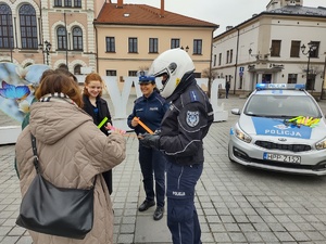 policjanci wręczający kobietą odblaski w tle radiowóz policyjne motocykle oraz rynek