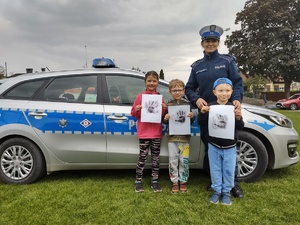 zdjęcie kolorowe policjantka i dzieci stoją przy radiowozie dzieci trzymają odciski linii papilarnych