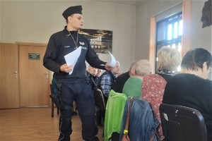 zdjęcie kolorowe policjant rozdaje ulotki seniorom którzy siedzą za stołem