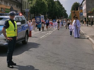 zdjęcie kolorowe na pierwszym planie stoi policjant widoczny też fragment radiowozu w tle procesja