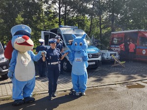 zdjęcie kolorowe policjanta z maskotkami na tle radiowozu