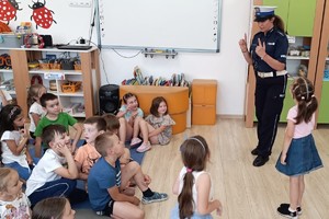 zdjęcie kolorowe policjantka prowadzi prelekcję obok niej stoi dziewczynka pozostałe dzieci siedzą