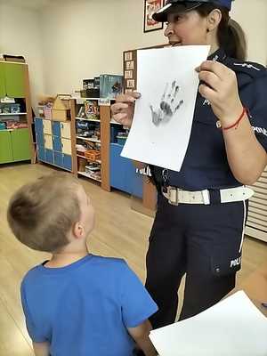 zdjęcie kolorowe policjantka pokazuje odbitki linii papilarnych obok tyłem stoi chłopczyk