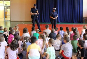 zdjęcie kolorowe zrobione w sali policjantka i policjant stoją obok siebie dzieci siedzą tyłem
