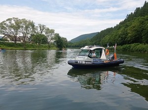 zdjęcie kolorowe, policyjna motorówka na jeziorze, widoczni płynący kajakarze, w tle góry