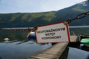 zdjęcie kolorowe na pierwszym planie tabliczka zawieszona na pomoście z napisem nieupoważnionym wstęp wzbroniony w tle pomost z rowerkami jezioro i góry