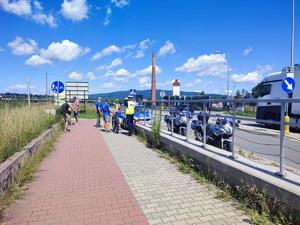 zdjęcie kolorowe zrobione z dalszej odległości. przedstawia trzech policjantów stojących obok radiowozu i policyjnych motocykli. w tle góry