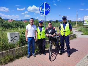 zdjęcie kolorowe przedstawiające dwoje policjantów ruchu drogowego obok których stoi przedstawiciel Caritas. Pomiędzy nimi rowerzystka. w tle znak drogowy droga dla rowerów