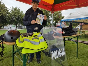 zdjęcie kolorowe policjantka na stoisku profilaktycznym w rękach trzyma książeczką z napisem bezpieczne wakacje