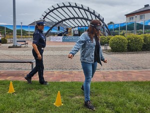 zdjęcie kolorowe kobieta w założonych alkogooglach pokonuje slalom obok policjantka