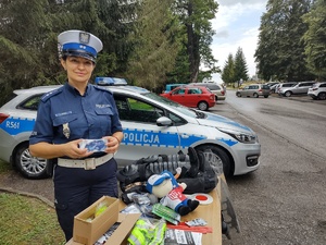 zdjęcie kolorowe policjantka stoi prze stoisku profilaktycznym w tle zaparkowane samochody