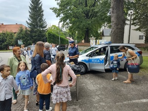 zdjęcie kolorowe stoisko policyjne przy którym stoją osoby obok zaparkowany radiowóz