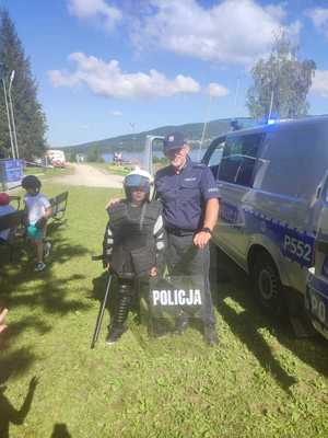 kolorowe zdjęcie policjanta obok którego stoi chłopczyk w policyjnym wyposażeniu