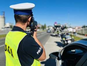 zdjęcie kolorowe policjant stoi tyłem podczas pomiaru prędkości w tle ulica