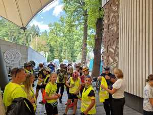 zdjęcie kolorowe przedstawiające policjanta i grupę rowerzystów w kamizelkach odblaskowych, w tle drzewa