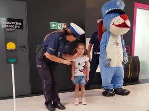 zdjęcie kolorowe, stojąca policjantka i dziecko, obok sygnalizator świetlny, z tyłu sznupek