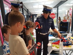 zdjęcie kolorowe przedstawiająca policjantów i dzieci stojących przy stoisku profilaktycznym