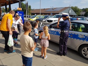 zdjęcie kolorowe zrobione na zewnątrz, policjantka stoi przy radiowozie, obok stoją dzieci