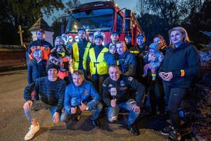 zdjęcie kolorowe grupowe przedstawiające stojących koło siebie policjantów, strażaków, ratowników oraz dziennikarzy, w tle wóz strażacki