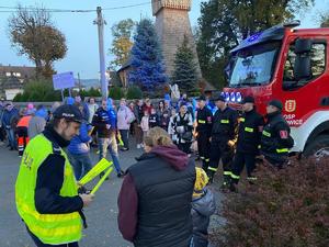 zdjęcie kolorowe przedstawiające policjanta rozdającego odblaski, w tle wóz strażacki