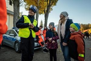 zdjęcie kolorowe przedstawiające policjantkę obok której stoi kobieta z dwóją dzieci, w tle ratownicy.