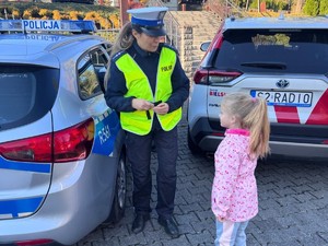 zdjęcie kolorowe przedstawiające policjantkę, obok niej stoi dziewczynka, obok radiowóz