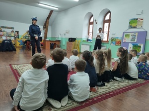 zdjęcie kolorowe policjantka stoi przed dziećmi dzieci siedzą na dywanie