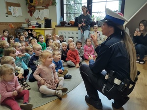 zdjęcie kolorowe policjantka kuca dzieci siedzą przed nią zdjęcie zrobione z boku