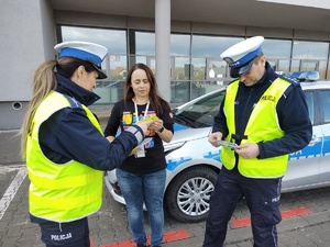 Zdjęcie kolorowe policjanci wręczają kobiecie odblaski w tle radiowóz