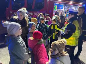 zdjęcie kolorowe, policjantka rozdaje odblaski dzieciom