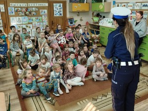 zdjęcie kolorowe, policjantka na środku sali, dzieci siedzą na podłodze