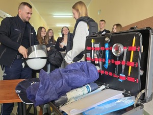 zdjęcie kolorowe na pierwszym planie walizka technika w tle uczestnicy i policjant