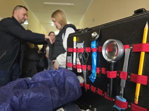 na pierwszym planie walizka technika kryminalistyki w tle uczniowie i policjant