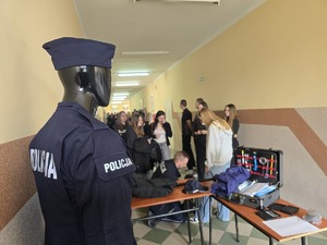 na pierwszym planie manekin w mundurze policyjnym w tle policjant i uczniowie podczas prezentacji sprzętu