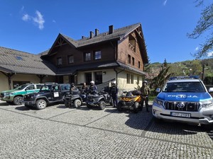 zdjęcie kolorowe zaparkowanych samochodów różnych służb obok stoją funkcjonariusze