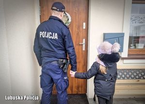 policjant stojący tyłem trzyma za rękę dziecko