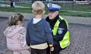 zdjęcie dzieci stojących tyłem i kucającego przed nimi policjanta