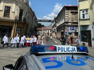 na pierwszym planie radiowóz w tle procesja