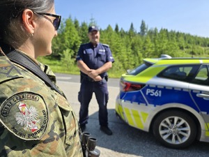 na pierwszym planie funkcjonariuszka straży granicznej w tle policjant i radiowóz
