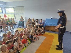 policjantka stoi przed dziećmi i prowadzi prelekcje dzieci siedzą
