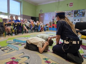 policjantka z dwoma chłopcami którzy pokazują jaką należy przyjąć pozycję w przypadku ataku groźnego psa
