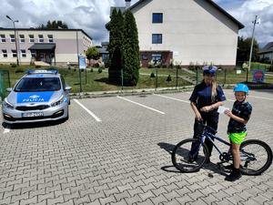 zdjęcie kolorowe, policjantka z rowerzystą, w tle szkoła i radiowóz