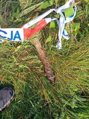 zdjęcie kolorowe, pocisk artyleryjski leżący w zaroślach