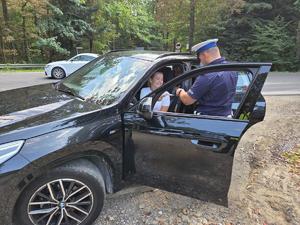 zdjęcie kolorowe, policjant rozdaje ulotkę kierującemu