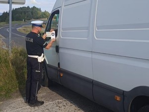 zdjęcie kolorowe, policjant rozdaje ulotkę kierującemu